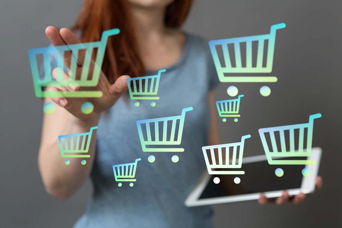 Žena drží v ruke tablet a druhou rukou sa dotýka virtuálnych ikon nákupných košíkov.