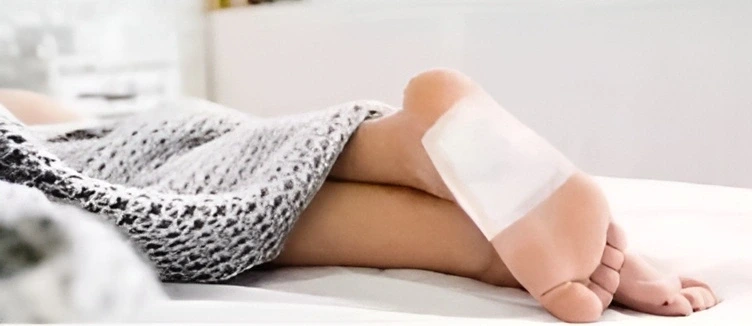 Chodidla s nalepenými detoxikačními náplastmi vyčnívající zpod deky.