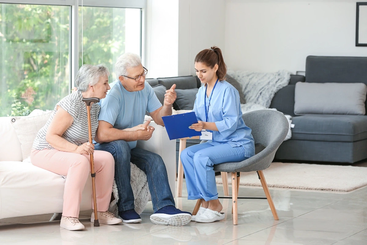 Dvojice seniorů poslouchá instrukce, které jim dává zdravotnická pracovnice.