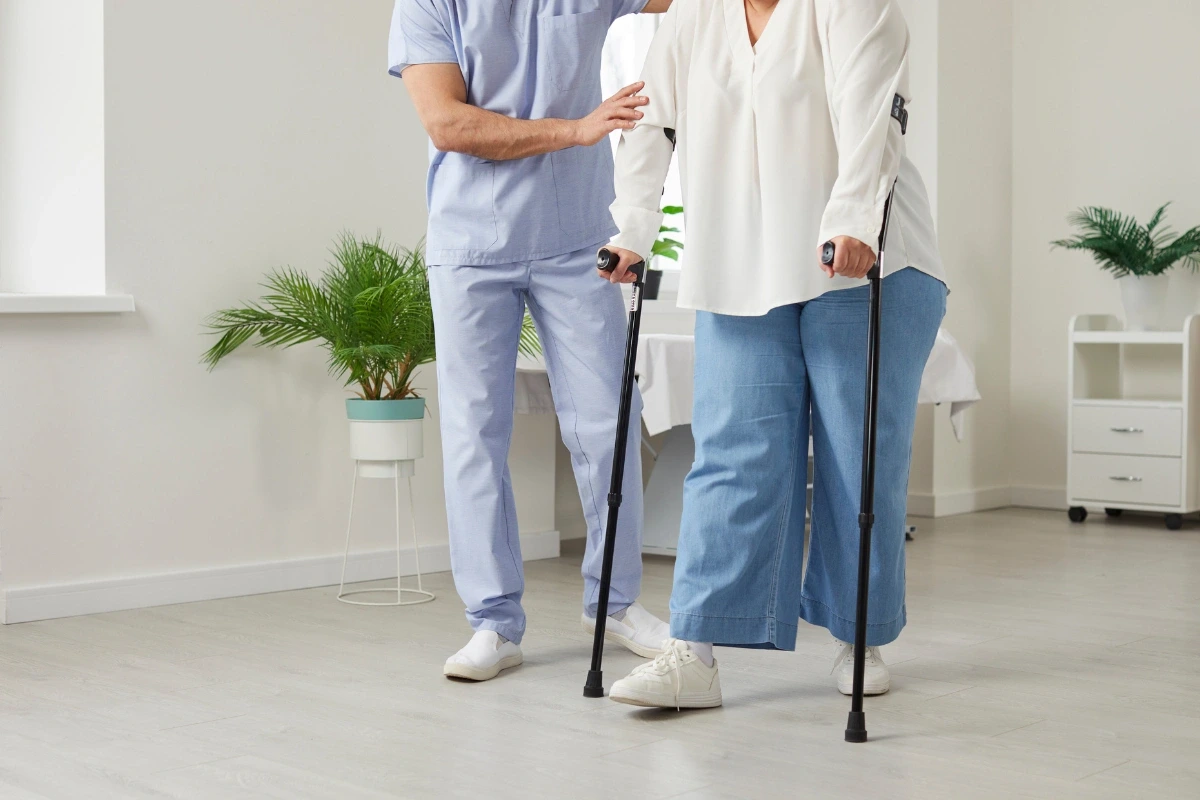 Pacientka s francouzskými berlemi za asistence zdravotníka.