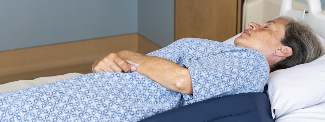Pacientka ležící na lůžku – péče a prevence proti proleženinám.